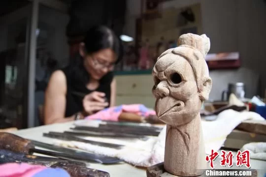 新雕刻出来的木偶头造型与正在埋头工作的“江加走木偶头”传承人相映成趣。 廖静 摄 “姐妹花”坚守“江加走木偶头”:用匠心传承古老技艺(图3)